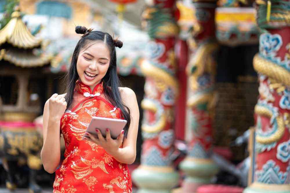 wanita asia memakai baju tradisional cina saat imlek sedang bahagia melihat tablet karena dapat untung bisnis
