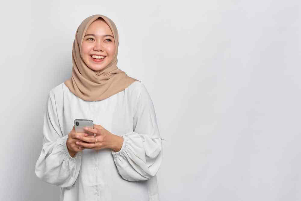wanita hijab pegang ponsel tersenyum bahagia